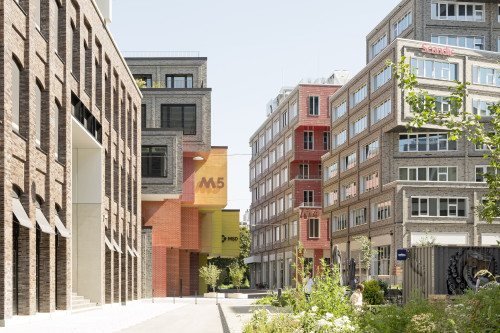 Eine moderne Stadtstraße mit mehrstöckigen Backstein- und Glasgebäuden, darunter eines mit einem gelben 