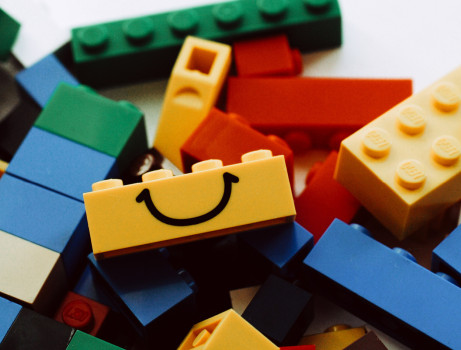 Ein Stapel bunter Spielzeugbausteine, davon ist ein gelber Baustein mit einem einfachen schwarzen Smiley bemalt.