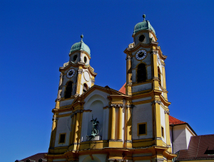 Kirche St. Michael Berg am Laim im Barockstil mit zwei hohen Glockentürmen und grünen Kuppeln vor strahlend blauem Himmel.