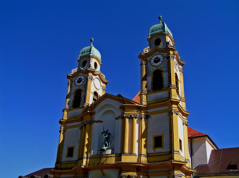 Kirche St. Michael Berg am Laim im Barockstil mit zwei hohen Glockentürmen und grünen Kuppeln vor strahlend blauem Himmel.