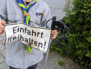 Eine Person in einer Pfadfinderuniform hält ein verbogenes Metallschild mit der Aufschrift 
