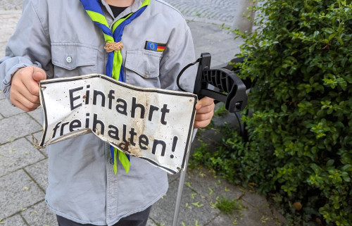 Eine Person in einer Pfadfinderuniform hält ein verbogenes Metallschild mit der Aufschrift 