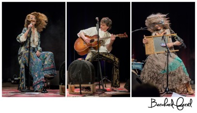 zwei Frauen und ein Mann spielen mit ihren Instrumenten sitzend auf einer Bühne. Der Mann spielt eine Gitarre, eine der Frauen spielt eine Zitter