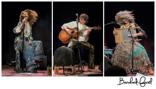 zwei Frauen und ein Mann spielen mit ihren Instrumenten sitzend auf einer Bühne. Der Mann spielt eine Gitarre, eine der Frauen spielt eine Zitter