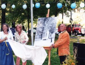 Drei Personen enthüllen ein großes Schwarz-Weiß-Foto auf einer Staffelei unter einem Straßenschild 