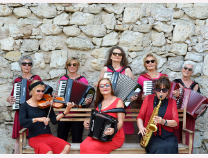 Sieben Frauen in roten und schwarzen Kleidern spielen Musikinstrumente, fünf Akkordeons, eine Geige und ein Saxophon, während sie vor einer Steinmauer posieren.