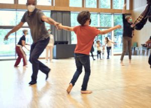 Kinder und Erwachsene tanzen in einem Saal.